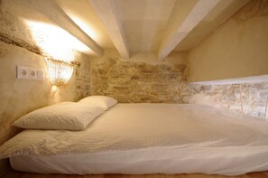 A bedroom with a stone wall, a bed with white bedding, and a wall-mounted light fixture. - 290 - Livingtarifa Catamaran (Tarifa)