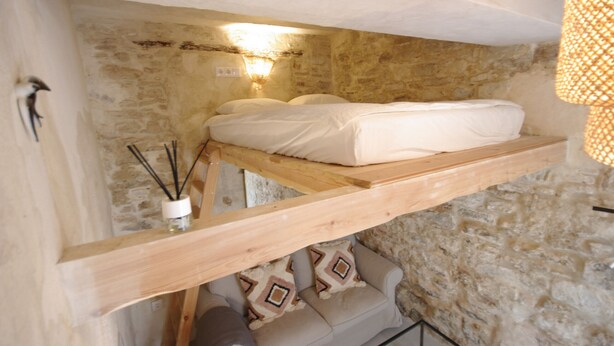 Dormitorio de piedra rústica con estructura de cama de madera, una mesita de noche y una lámpara colgante.