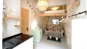 Un espacio habitable compacto con kitchenette, un sofá con cojines estampados, una lámpara colgante y una pared de piedra rústica.