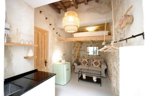 A compact living space with a kitchenette, a sofa with patterned cushions, a hanging light fixture, and a rustic stone wall.