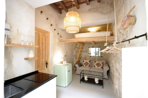 A compact living space with a kitchenette, a sofa with patterned cushions, a hanging light fixture, and a rustic stone wall. - 290 - Livingtarifa Catamaran (Tarifa)