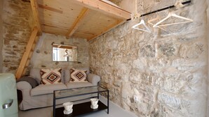 Una habitación con pared de piedra, techo de madera, sofá con cojines estampados, mesa de centro de vidrio y lámpara colgante.