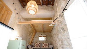 Una habitación rústica con pared de piedra, techo de madera, refrigerador verde claro, sofá con cojines estampados e lámpara colgante.