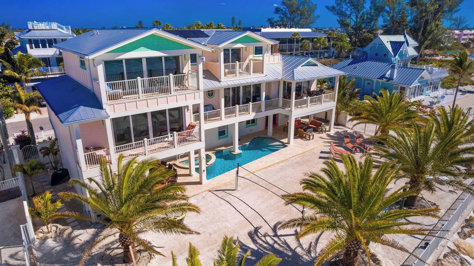 A multi-story beachfront property with a swimming pool, balconies, and palm trees.