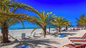 Une plage bordée de palmiers, avec des chaises longues et une clôture le long du rivage.