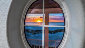 Une fenêtre donnant sur un coucher de soleil sur l’océan et une plage.