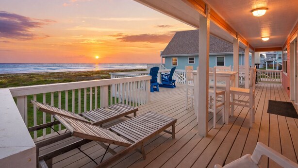 A wooden deck with lounge chairs and a view of the sunset over the ocean.