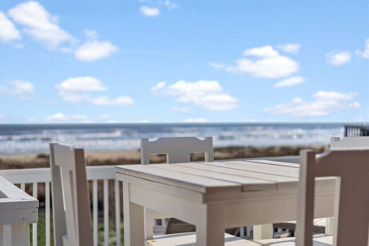 A white wooden table and chairs set outdoors with a view of the ocean.