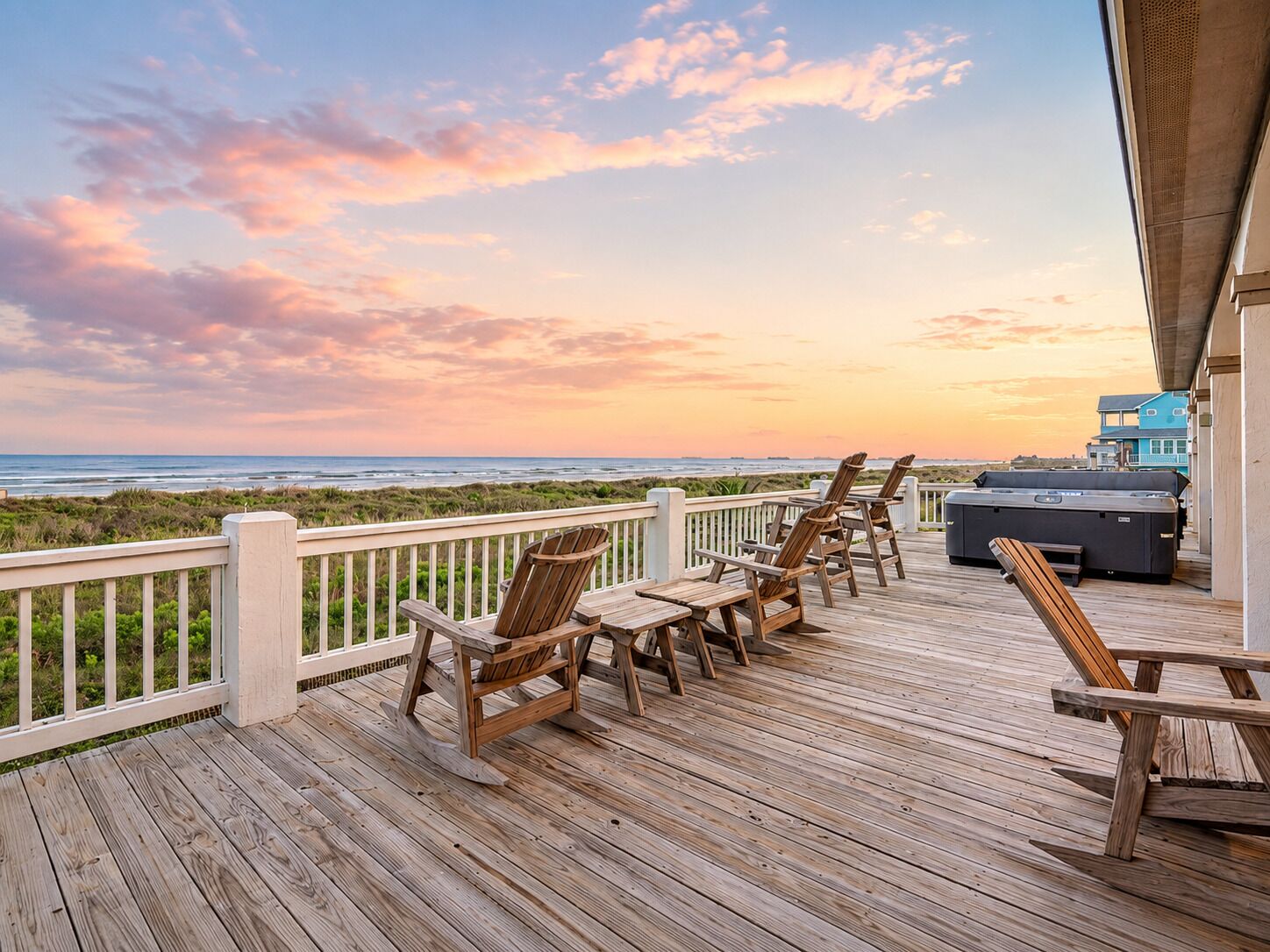 A wooden deck with outdoor seating and a hot tub overlooking a beach at sunset.