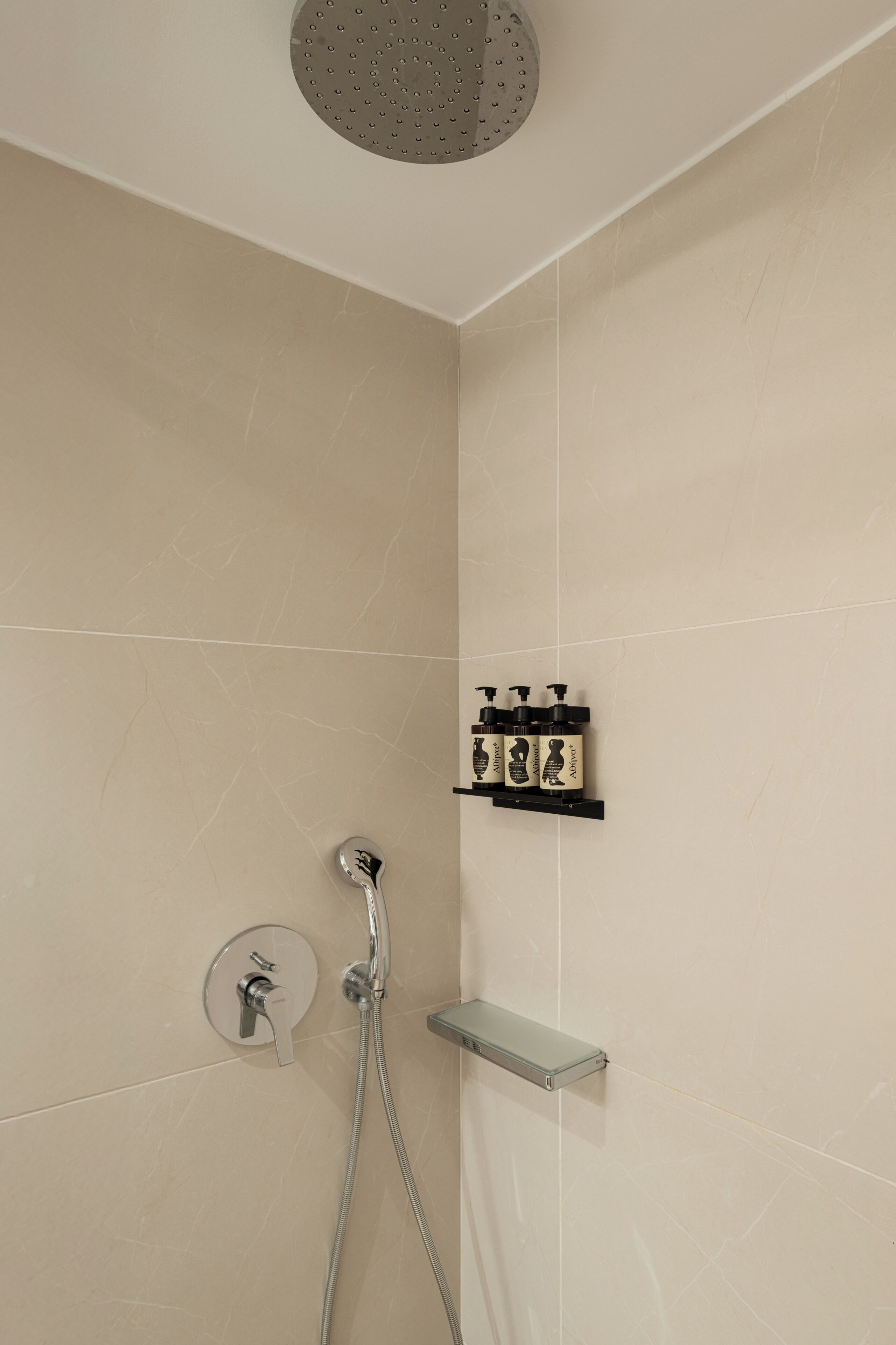 A shower area with a handheld showerhead, a wall-mounted faucet, and a shelf with toiletries.