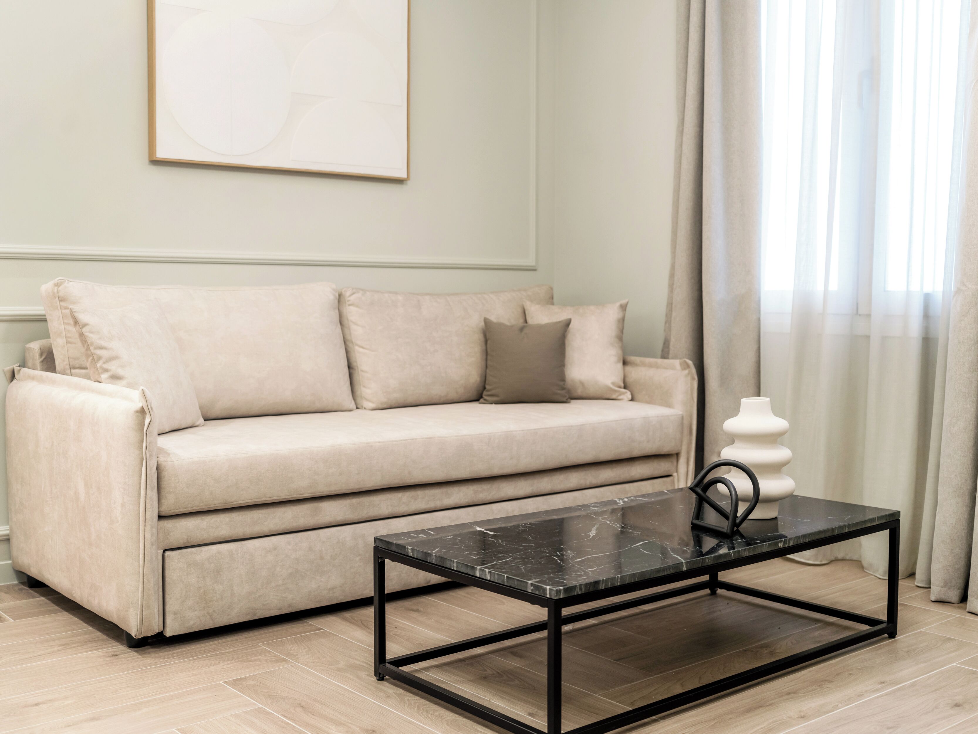 Een beige bank met een zwart metalen salontafel in een kamer met licht houten vloeren.