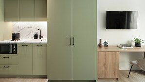 Uma cozinha moderna com armários verdes, painel de backsplash de mármore e uma televisão de tela plana fixada na parede.