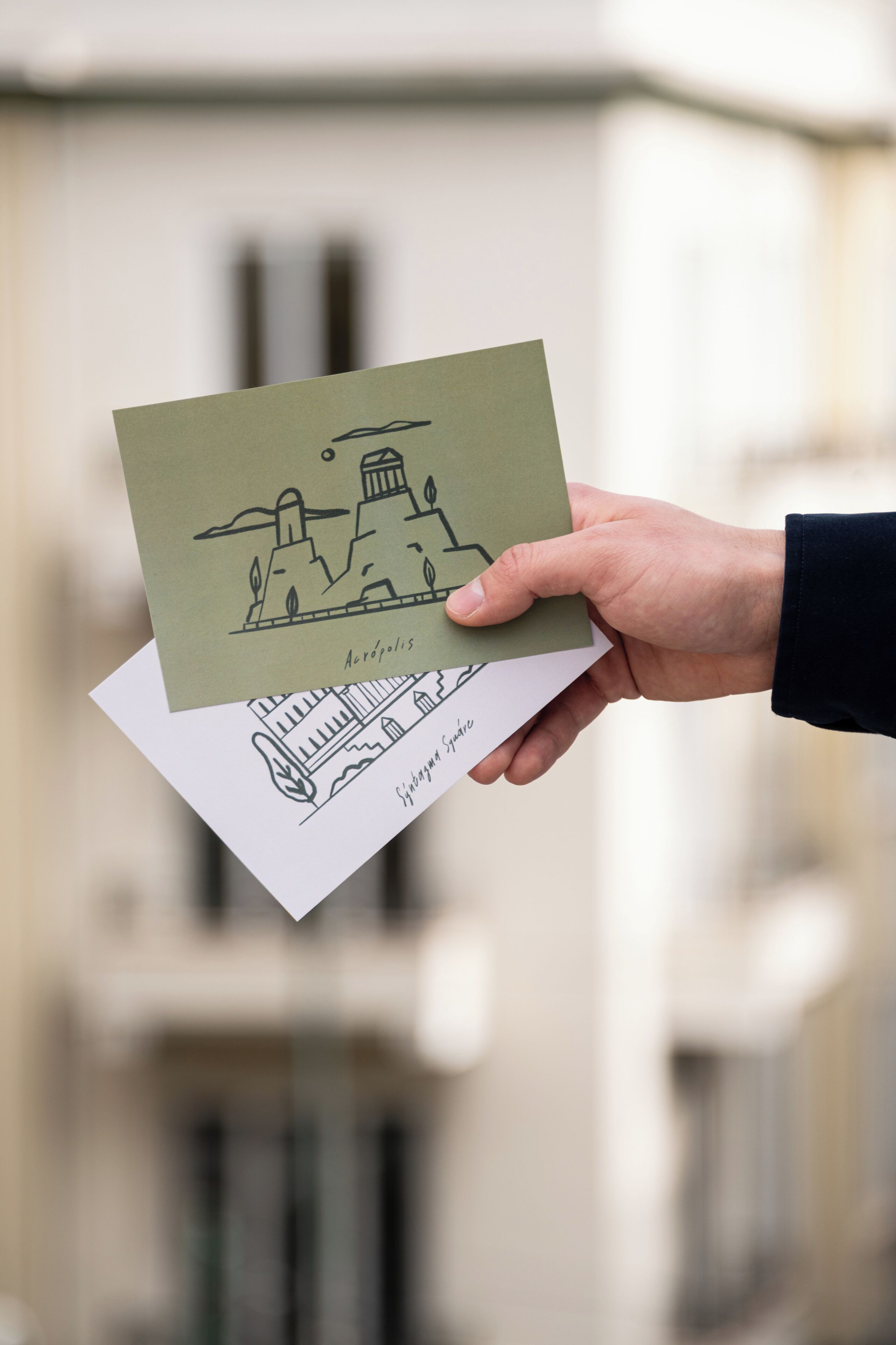 A hand holding a postcard with a drawing of a building labeled "Aphrodisias."