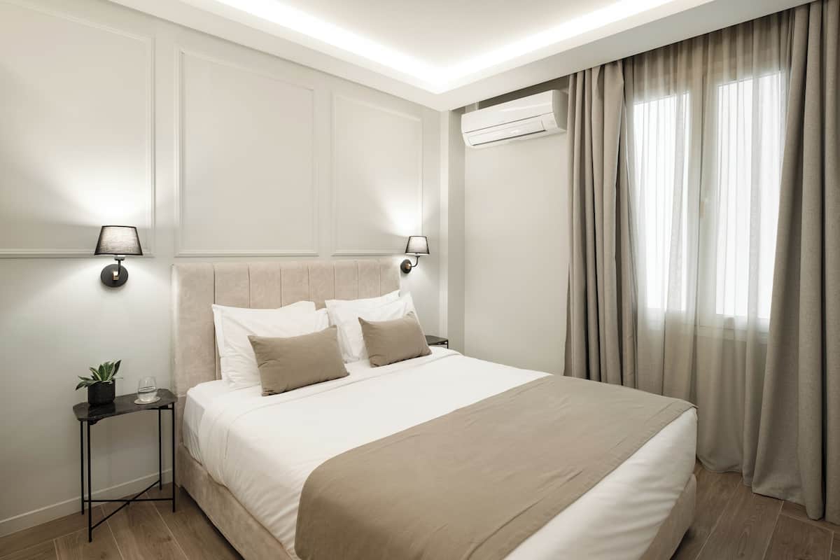 Ein modernes Hotelzimmer mit einem großen Bett, Nachttischlampen, einem kleinen Tisch mit einer Pflanze und einer Klimaanlage.