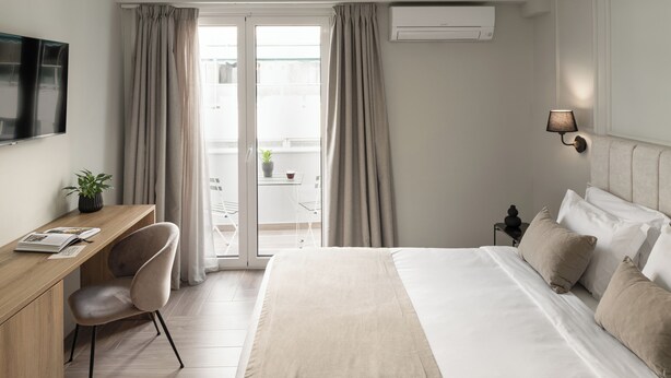 Quarto de hotel moderno com cama, escrivaninha, cadeira e televisão.