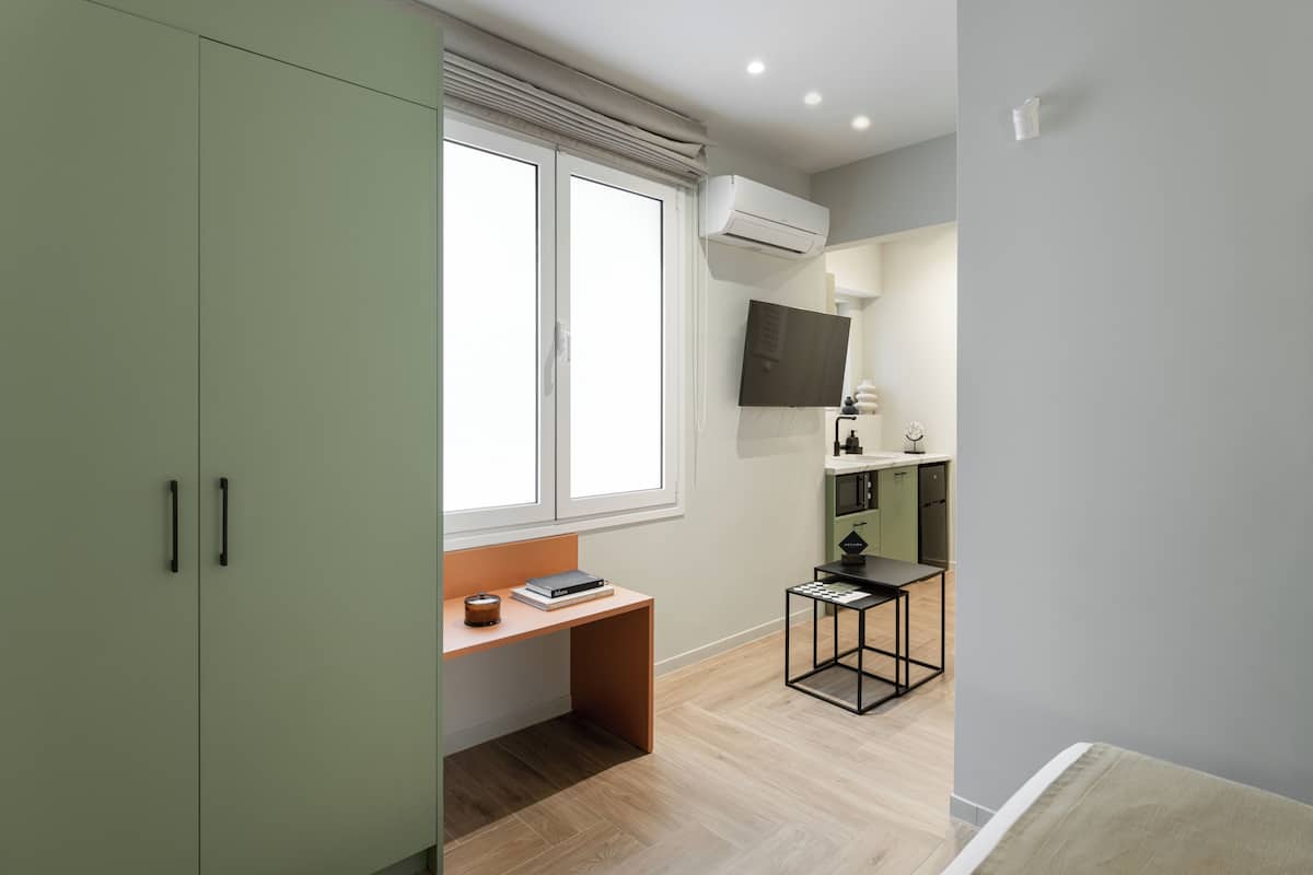 Ein modernes Zimmer mit Schreibtisch, Wandfernseher und einer Küchenzeile.