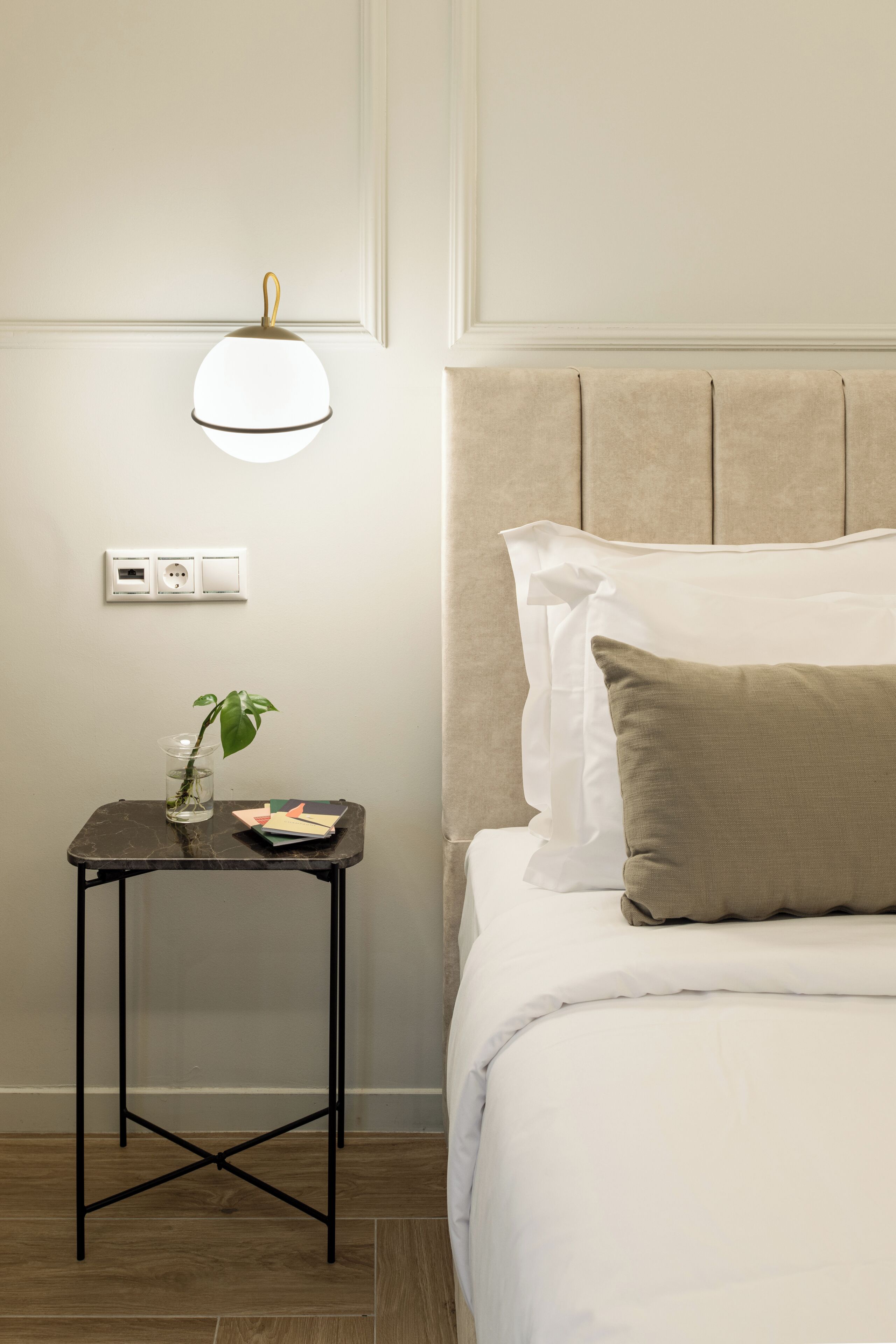 En pænt redt seng med et sengegærde, et natbord med en lampe, og en stikkontakt på væggen.