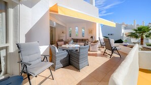 An outdoor patio with wicker furniture, a table, and a yellow awning. - E04 Jardines 1 - Apartment (Sitio de Calahonda)