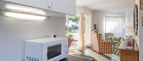 A kitchen with a microwave, a dining area with a chair, a lamp, and a view of the outdoors.