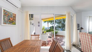 A dining area with a wooden table and chairs, a sofa, and a view of the outdoors. - L02 Jardines 1 - Apartment (Sitio de Calahonda)