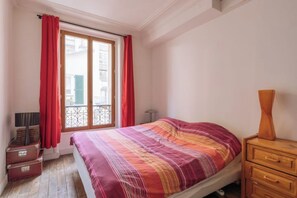 A bedroom with a bed, a nightstand, a lamp, and a window with curtains. - Superbe Appartement Parisien pour 3 - Belleville (Paris)