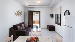 Una sala moderna con un sofá, una mesa de comedor con fruteros, una mesa auxiliar y un refrigerador.