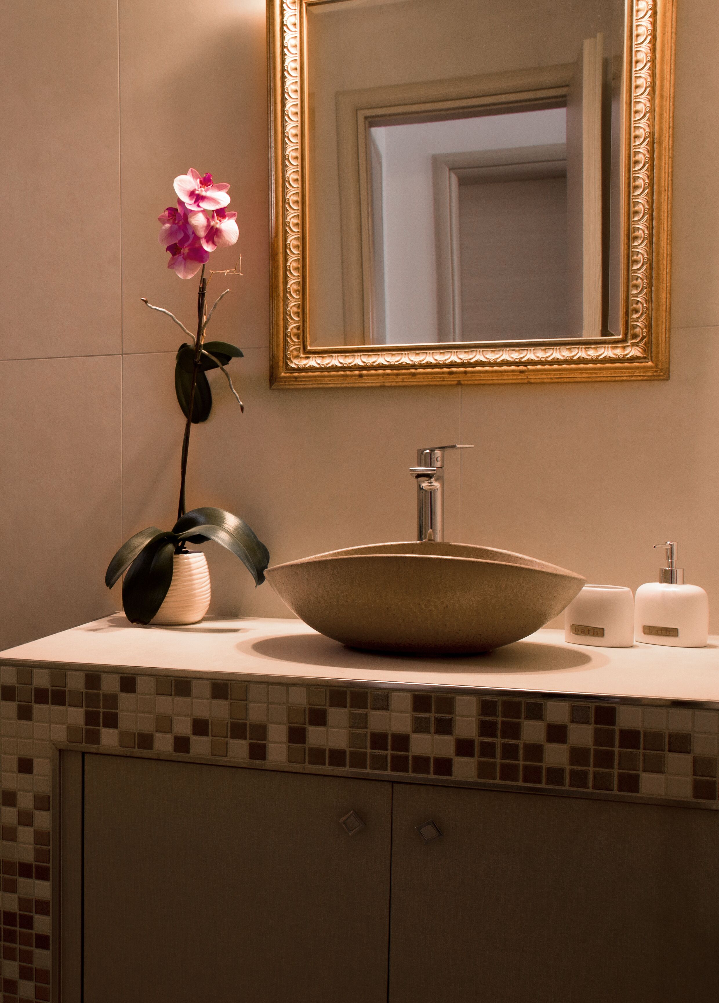 A bathroom vanity with a large mirror, a bowl sink, a potted orchid, and toiletries.