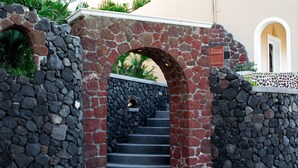 Una escalera de piedra que conduce a la entrada de un edificio, rodeada de muros de piedra y vegetación.