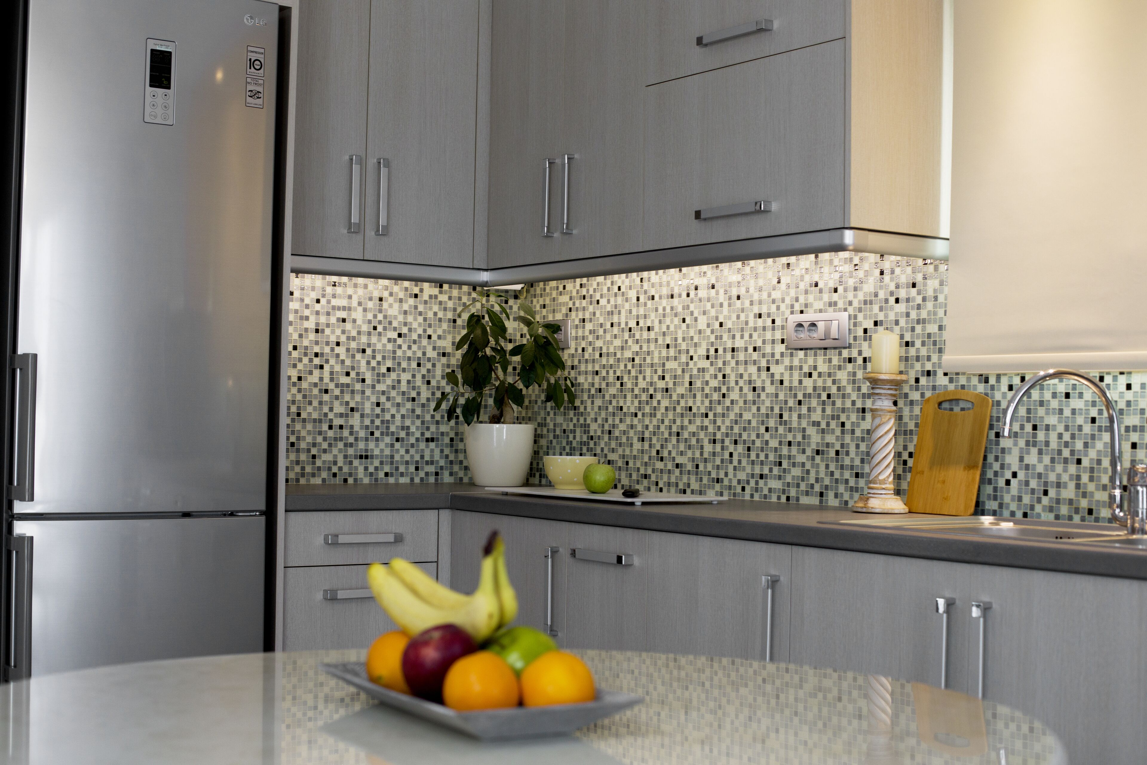 A modern kitchen with grey cabinets, a stainless steel refrigerator, a tiled backsplash, and a fruit bowl on the counter.
