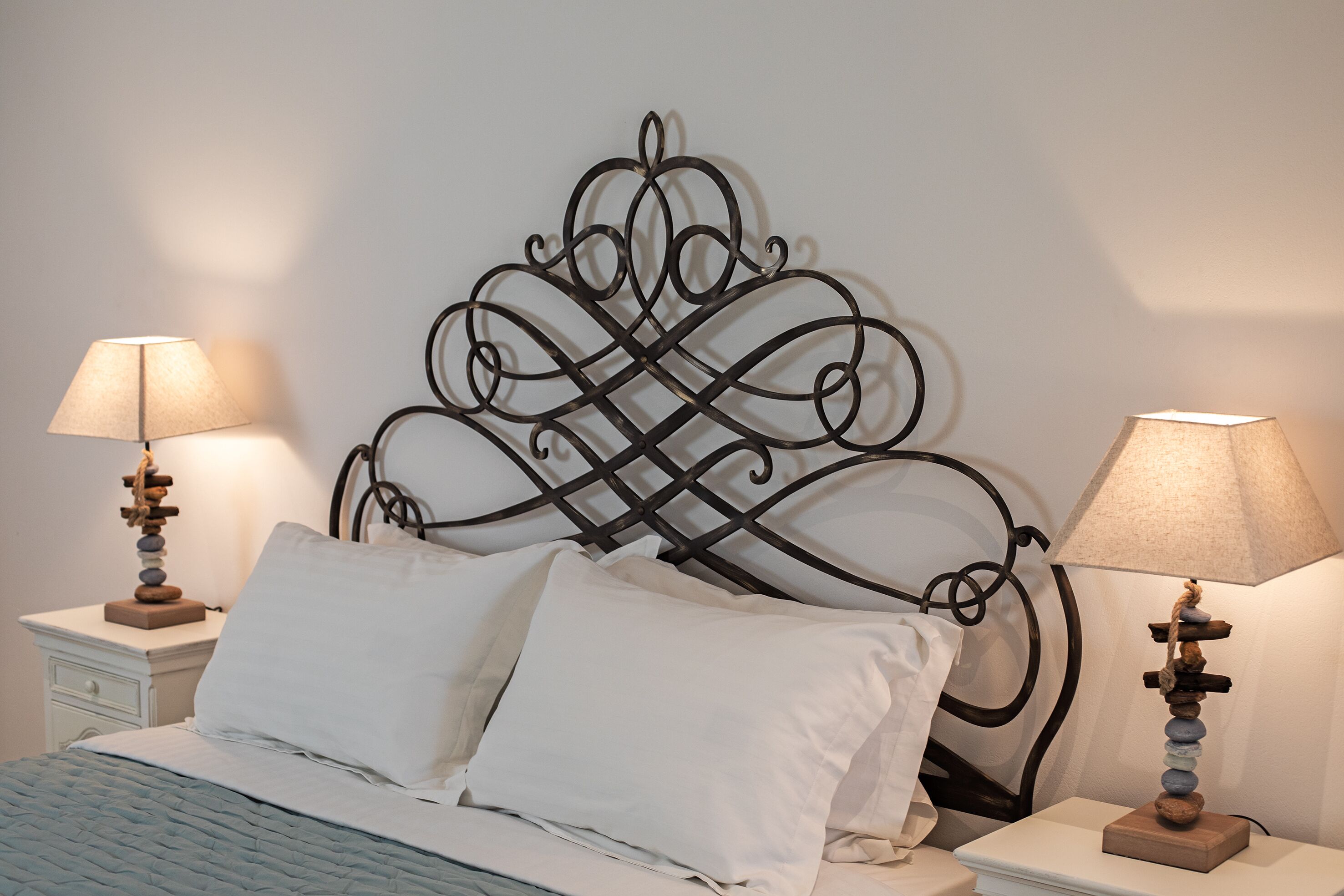 A neatly made bed with white linens, a decorative metal headboard, and two bedside lamps with lampshades.