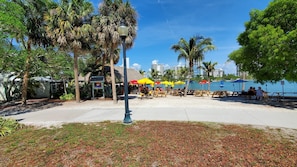 Zona de playa con mesas de picnic, sombrillas y palmeras.