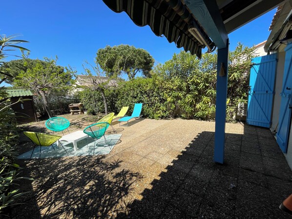 Un espace extérieur abrité, doté d’une terrasse en gravier, d’une table avec des chaises et d’un portail bleu.
