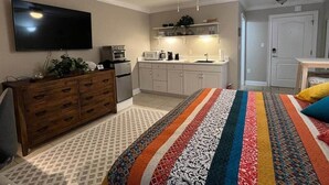 Ein Schlafzimmer mit Bett, Schminktisch, Fernseher, Deckenventilator und einer Küchenzeile.