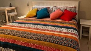 Ein Bett mit einer farbenfrohen Bettdecke, ein Gemälde an der Wand und eine Lampe.