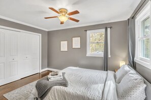 A bedroom with a bed, a ceiling fan, a window with curtains, and framed pictures on the wall. - Hickory Haven (Mauldin)