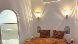 Een slaapkamer met een groot bed, twee bedlampen, een airconditioner en uitzicht op een balkon.