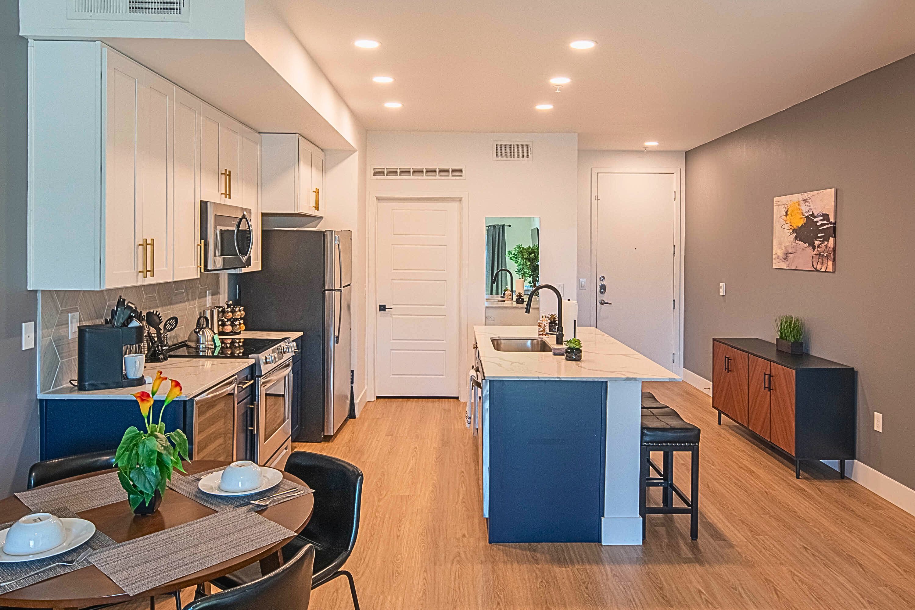 A modern kitchen with white cabinets, a central island, and a dining area with a table and chairs.
