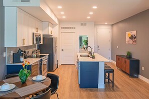 A modern kitchen with white cabinets, a central island, and a dining area with a table and chairs.