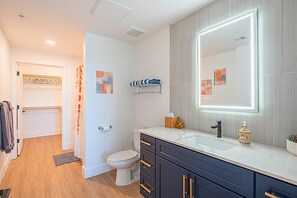 A modern bathroom with a white toilet, black cabinets, a large mirror, and a marble countertop.