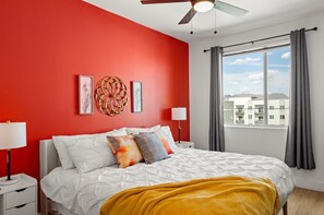 A bedroom with a red wall, a bed with white bedding, a yellow throw blanket, and a window with curtains.