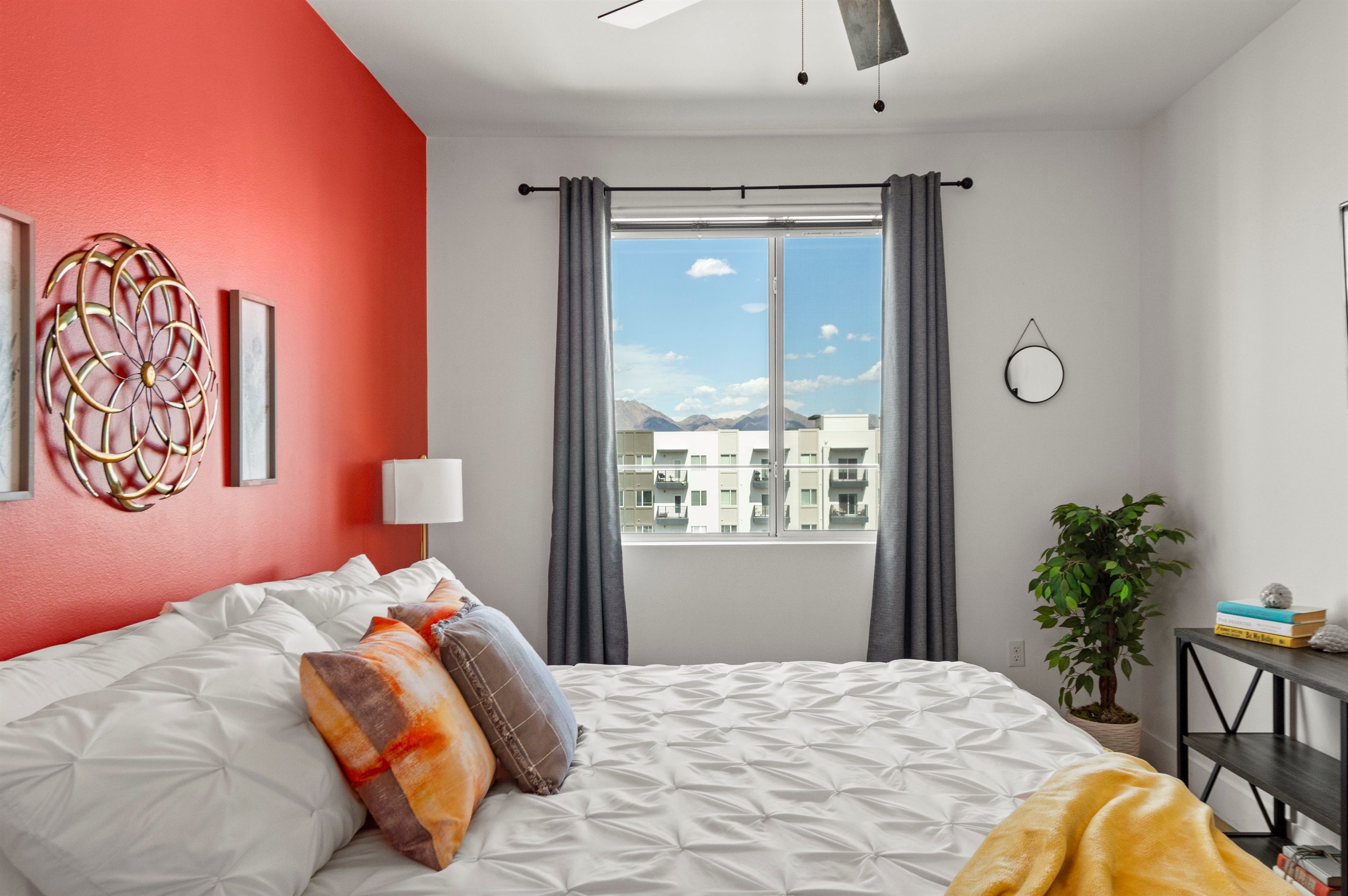 A bedroom with a bed, a potted plant, a bedside table, and a window with curtains.