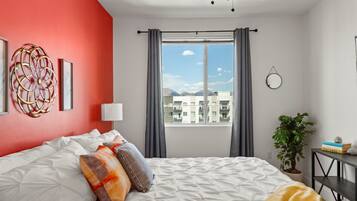 A bedroom with a bed, a potted plant, a bedside table, and a window with curtains.
