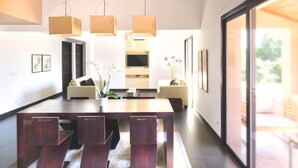 Un espace repas moderne avec une table en bois, des luminaires suspendus et une vue sur l’extérieur grâce à une porte vitrée.