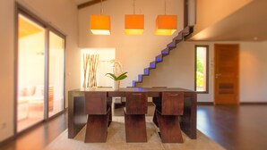 Un espace repas moderne avec une table et des chaises en bois foncé, un vase rempli de fleurs et un escalier illuminé de lumières bleues.