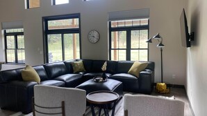 Ein modernes Wohnzimmer mit einem Ecksofa, zwei Sesseln, einem Couchtisch und großen Fenstern mit Blick auf einen Garten.
