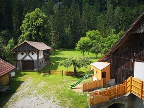 Entorno rural con un granero de madera, una casa pequeña y un parque infantil con un tobogán.