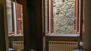 Ein Badezimmer mit Glaswaschtisch, Spiegel, Heizkörper und einem Fenster mit Holzklappläden.