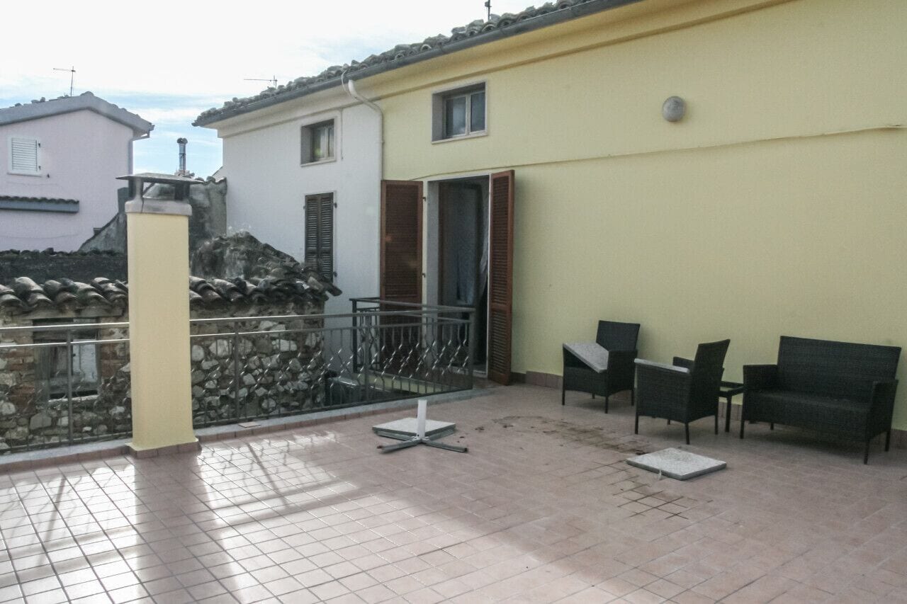 A balcony with a tiled floor, a small table, two chairs, and a sofa.