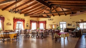 Uma sala de jantar ampla com vigas de madeira, várias mesas e cadeiras.