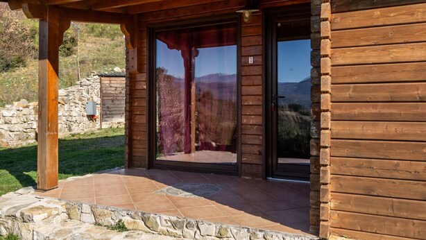 Uma cabana de madeira com parede de pedra e porta de vidro que dá para um pátio.